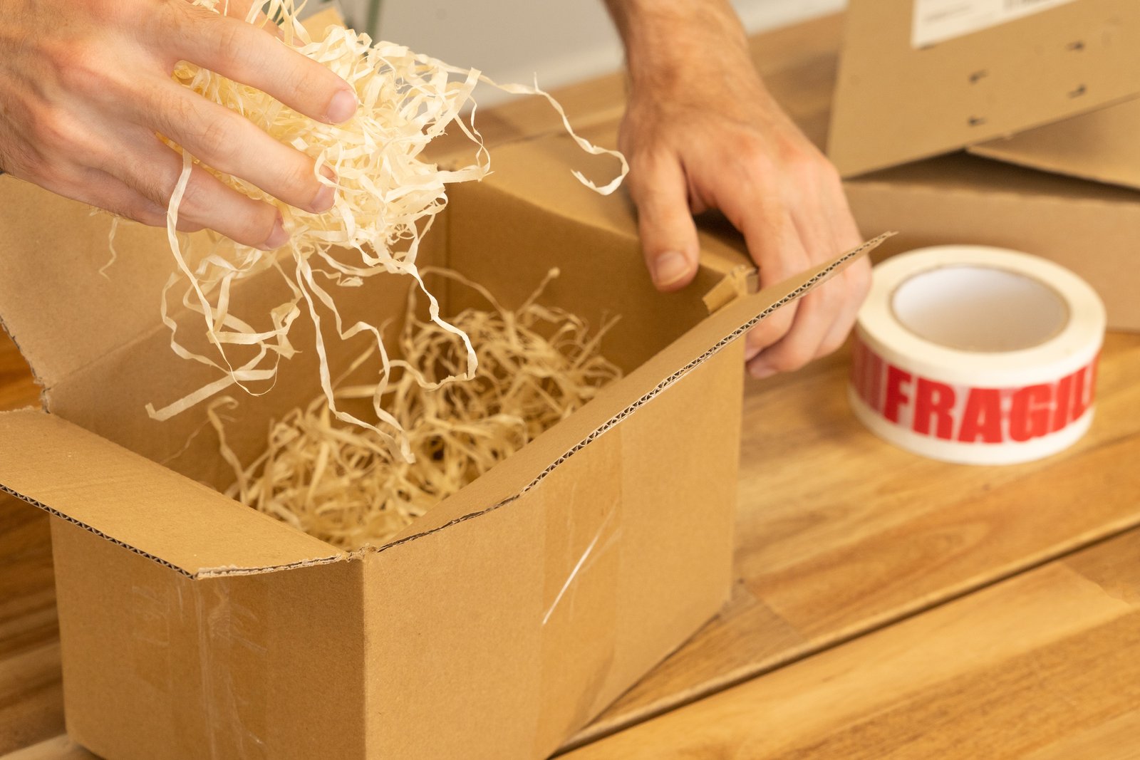 A cardboard shipping box being packed with protective wood wool for a fragile item