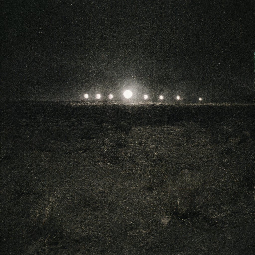 Illustration of a dark desert plain at night with distant glowing orbs hovering above the scrub, mountains on the horizon, deserted, no people