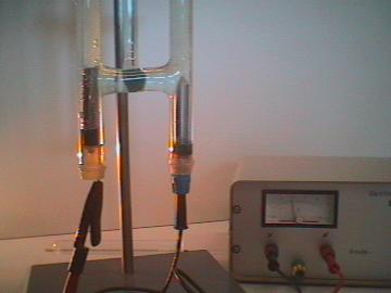 A laboratory demonstration of water electrolysis, showing hydrogen and oxygen gas collecting in graduated tubes above two electrodes